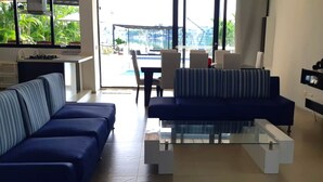 Un soggiorno moderno con divano, tavolino in vetro e vista su piscina e area relax all'aperto.
