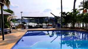 Una piscina con lettini e ombrelloni, circondata da palme e vista su un lago.