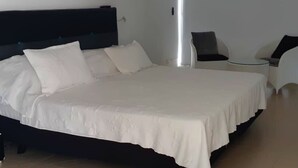 Un letto rifatto con lenzuola bianche in una stanza moderna, con una testiera scura e un comodino.