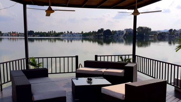 Un'area salotto esterna riparata con vista su un lago tranquillo e edifici in lontananza.