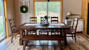 A dining area with a wooden table, chairs, a chandelier, and a view of the outdoors through large windows. - Spacious Mountain Cabin w/ Hot Tub & Bunkhouse (Donnelly)