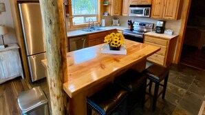 A kitchen with wooden cabinets, a stainless steel refrigerator, a microwave, and a wooden island with a vase of sunflowers. - Spacious Mountain Cabin w/ Hot Tub & Bunkhouse (Donnelly)