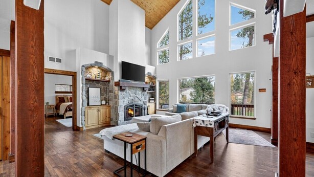 A spacious living room with a fireplace, wooden floors, and large windows. - Luxurious Cabin with Hot Tub, Large Yard, Fire Pit (Donnelly)