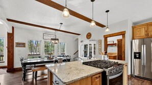 A modern kitchen with a central island, wooden cabinets, stainless steel appliances, and pendant lighting. - Luxurious Cabin with Hot Tub, Large Yard, Fire Pit (Donnelly)