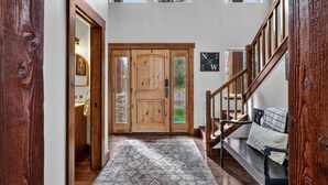 A wooden front door with a glass panel, a staircase with wooden railings, and a patterned rug on the floor. - Luxurious Cabin with Hot Tub, Large Yard, Fire Pit (Donnelly)