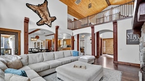 A spacious living area with a large sectional sofa, a dining table, and a kitchen in the background. - Luxurious Cabin with Hot Tub, Large Yard, Fire Pit (Donnelly)