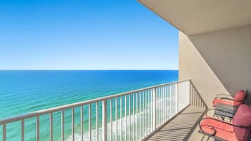 A balcony with a view of the ocean, a railing, and two red chairs.
