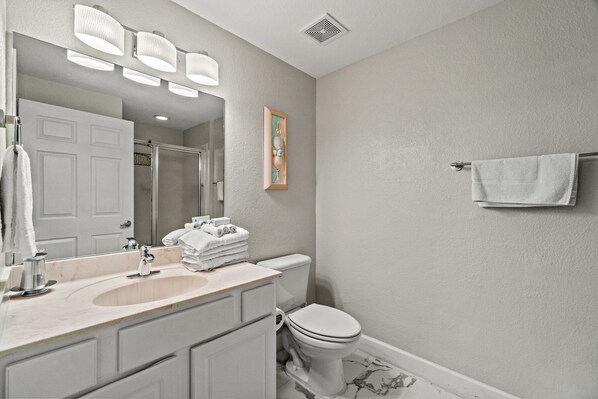 Une salle de bain avec un lavabo, un miroir et des toilettes. Des serviettes sont pliées sur le lavabo et un tableau encadré est accroché au mur.