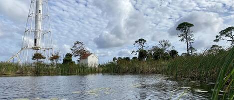 Un faro, un edificio blanco y una masa de agua con nenúfares.