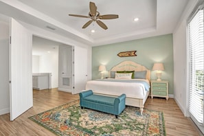 A bedroom with a bed, bedside tables, a ceiling fan, a rug, and a view of the outside.