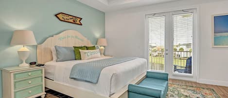 A bedroom with a bed, bedside tables, a bench, a window with blinds, and a view of the outdoors.