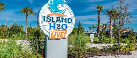 Un letrero de Island H2O con diseño de ola, rodeado de follaje y palmeras.
