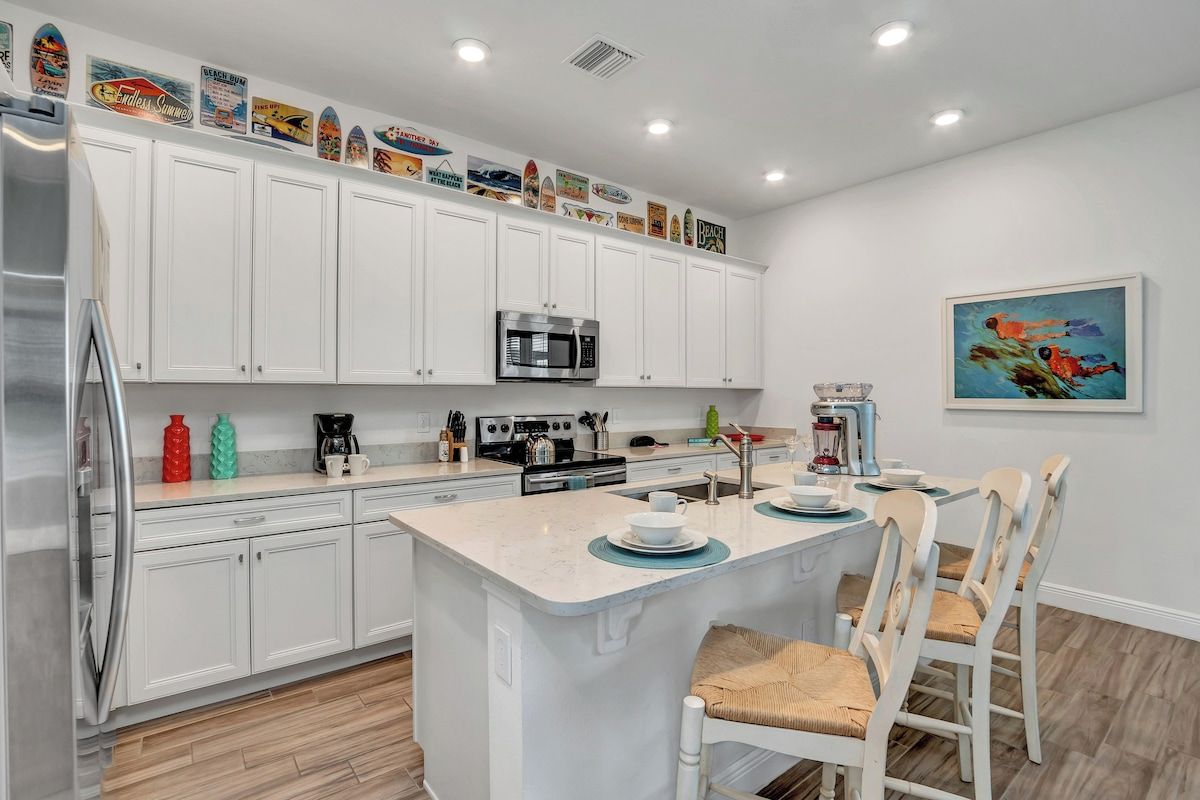 Una cocina moderna con armarios blancos, una isla central y un comedor con sillas blancas.