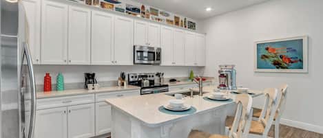 Una cocina moderna con armarios blancos, una isla central y un comedor con sillas blancas.