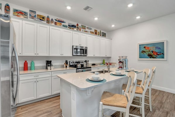A modern kitchen with white cabinetry, a central island, and a dining area with white chairs.