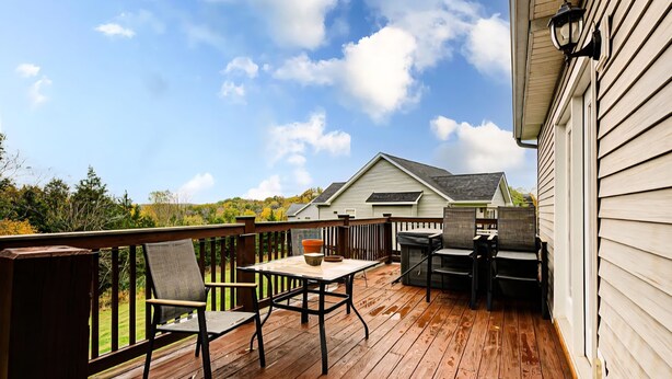 A wooden deck with a table and chairs, a view of a house, and a clear sky.