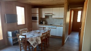 Eine kompakte Küche mit weißen Schränken, einer Mikrowelle, einem Backofen und einer Kaffeemaschine. Ein Esstisch mit Stühlen und ein Fenster sorgen für natürliches Licht.