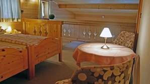 A wooden cabin room with a bed, a table with a lamp, and a chair.