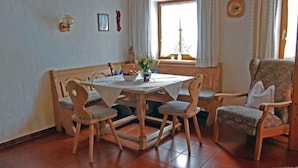 A dining area with a wooden table and chairs, a window with curtains, and a clock on the wall.