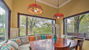 A dining area with a wooden table and chairs, a bench with patterned cushions, and large windows with a view of trees. - Dock, Hot Tub & Kayaks: Luxe Hot Springs Lakehouse (Hot Springs)
