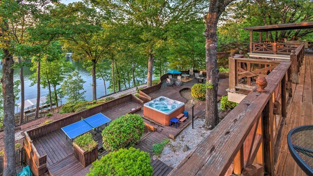A wooden deck with a hot tub, seating area, and a ping pong table overlooking a lake. - Dock, Hot Tub & Kayaks: Luxe Hot Springs Lakehouse (Hot Springs)