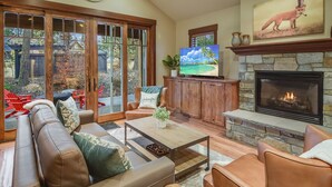 A cozy living room with a stone fireplace, a television, and a large window overlooking a backyard. - 1PM Check In/Out | A Suncadia Escape Where Nothing Feels Rushed! (Cle Elum)