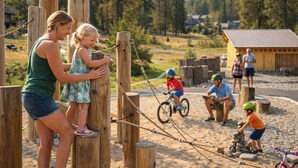 A wooden play structure in a park with a dirt path, surrounded by trees and a small building. - 1PM Check In/Out | A Suncadia Escape Where Nothing Feels Rushed! (Cle Elum)