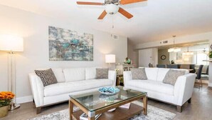 A modern living room with a glass coffee table, white sofas, and a ceiling fan. - Amazing view in Aventura! Cozy 2 BD at the Yacht Club (Aventura)