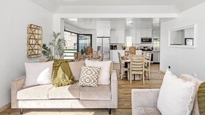 A modern living room with a sofa, a dining table, and a kitchen in the background. - Single Family Tranquil Beachfront Rental P1829-0 (Oceanside)