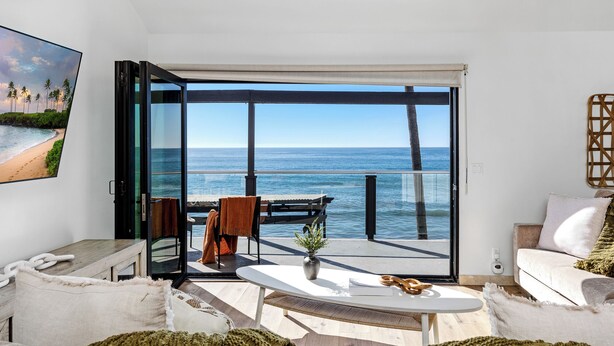 A modern living room with a large sliding glass door leading to a balcony with a view of the ocean. - Single Family Tranquil Beachfront Rental P1829-0 (Oceanside)