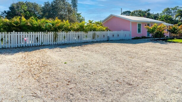 A pink house with a white picket fence, surrounded by gravel and greenery. - WATER SLIDE & POOL ** SUGAR SHACK** (Bradenton)
