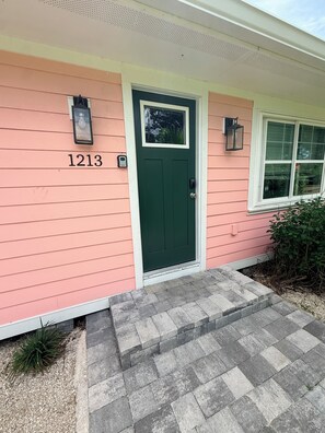 A house with a green door, a number '1213' on the wall, and two wall-mounted light fixtures.