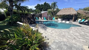 A swimming pool with lounge chairs and a thatched-roof structure. - WATER SLIDE & POOL ** SUGAR SHACK** (Bradenton)