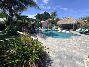 A swimming pool with lounge chairs and a thatched-roof structure. - WATER SLIDE & POOL ** SUGAR SHACK** (Bradenton)