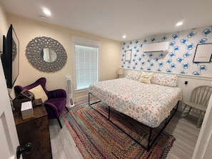 A bedroom with a bed, a dresser, a chair, a mirror, and a window with blinds.
