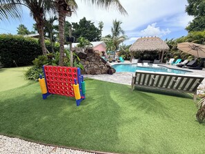 A pool area with a thatched-roof structure, lounge chairs, and a play structure.