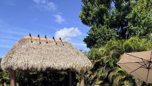 A clear swimming pool with lounge chairs and a thatched-roof structure. - WATER SLIDE & POOL ** SUGAR SHACK** (Bradenton)