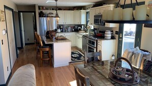 A spacious kitchen with a central island, wooden chairs, a dining table with a glass top, and a view of the outdoors. - Private mountainside chalet bordering Dolly Sods with beautiful panoramic view. (Davis)