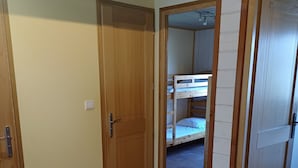 Una habitación con puerta de madera, suelo de baldosas y una cama litera al fondo.