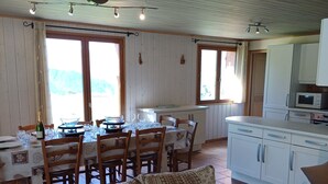 Un comedor acogedor con una mesa y sillas de madera, un sofá con cojines estampados, y una cocina con armarios blancos y un microondas.
