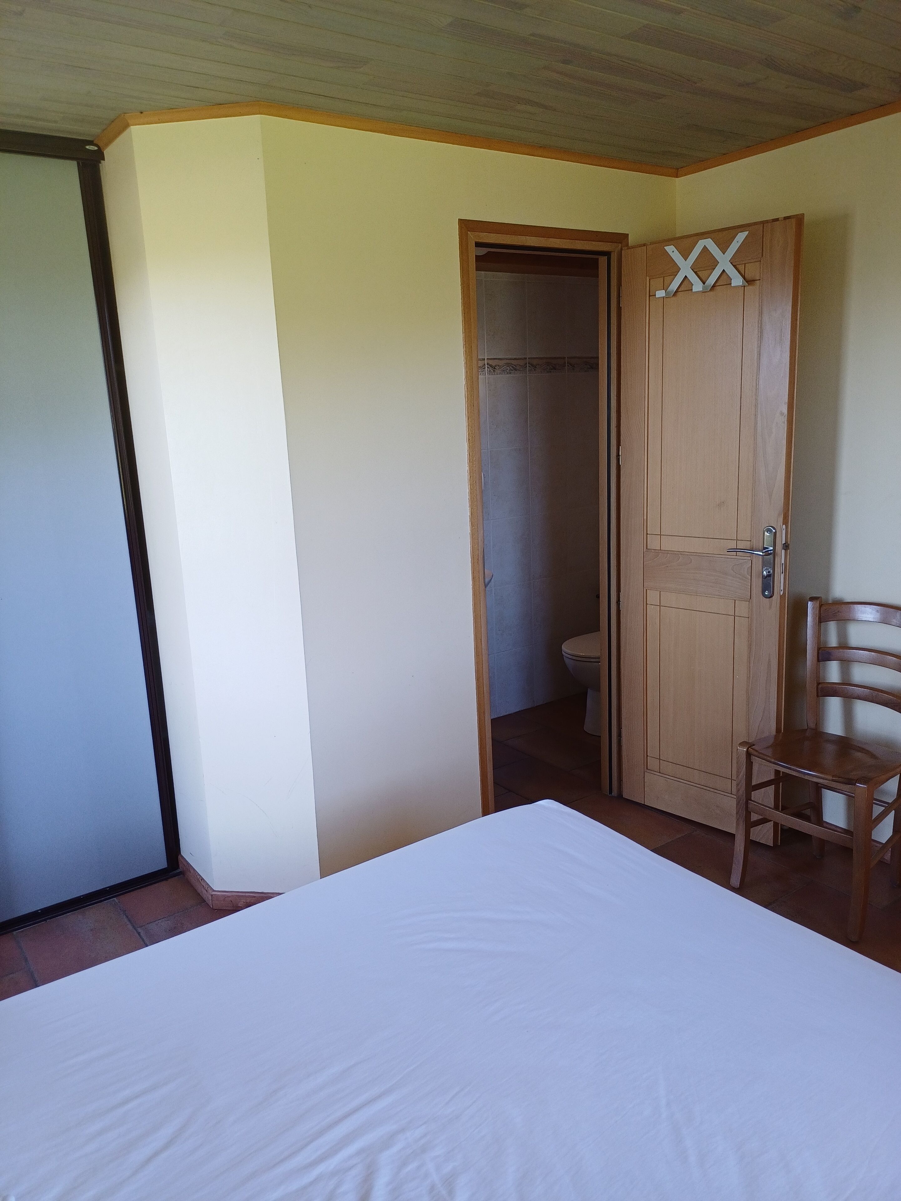Une chambre avec une porte en bois, une chaise en bois et un lit blanc.