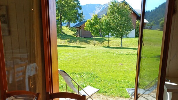 Una mesa de comedor dispuesta con platos, vasos y cubiertos, con vista a un jardín césped y edificios al fondo.
