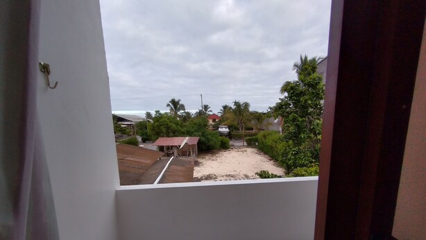 Vue depuis un balcon donnant sur une zone sablonneuse, avec une petite construction et de la végétation.