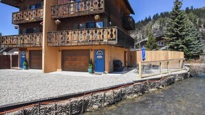A wooden chalet with a balcony, a gravel driveway, and a wooden deck by a clear water body. - River Rider at Brookside (Red River)