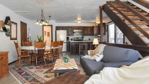 A modern kitchen with wooden cabinets, a dining area with a table and chairs, and a staircase leading to an upper level. - River Rider at Brookside (Red River)
