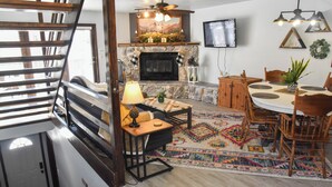 A cozy living room with a fireplace, wooden furniture, and a TV mounted on the wall. - River Rider at Brookside (Red River)