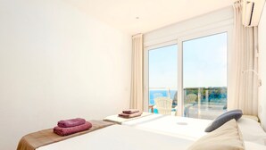 Ett hotellrum med en stor säng, ett litet bord med en stol och en balkong med utsikt över havet.