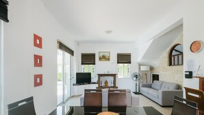 A modern living room with a glass dining table, a sofa, and a television. - Chrysanthemum Villa (Neo Chorio)