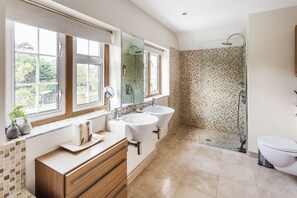 Features a spacious bathroom with two sinks, walk-in shower, and toilet, offering views of the surrounding area.
