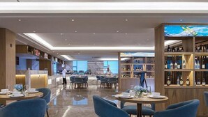 A modern restaurant with round tables and blue chairs, a bar area with shelves of bottles, and a chef preparing food. - Kyriad Marvelous Hotel (Dongguan)